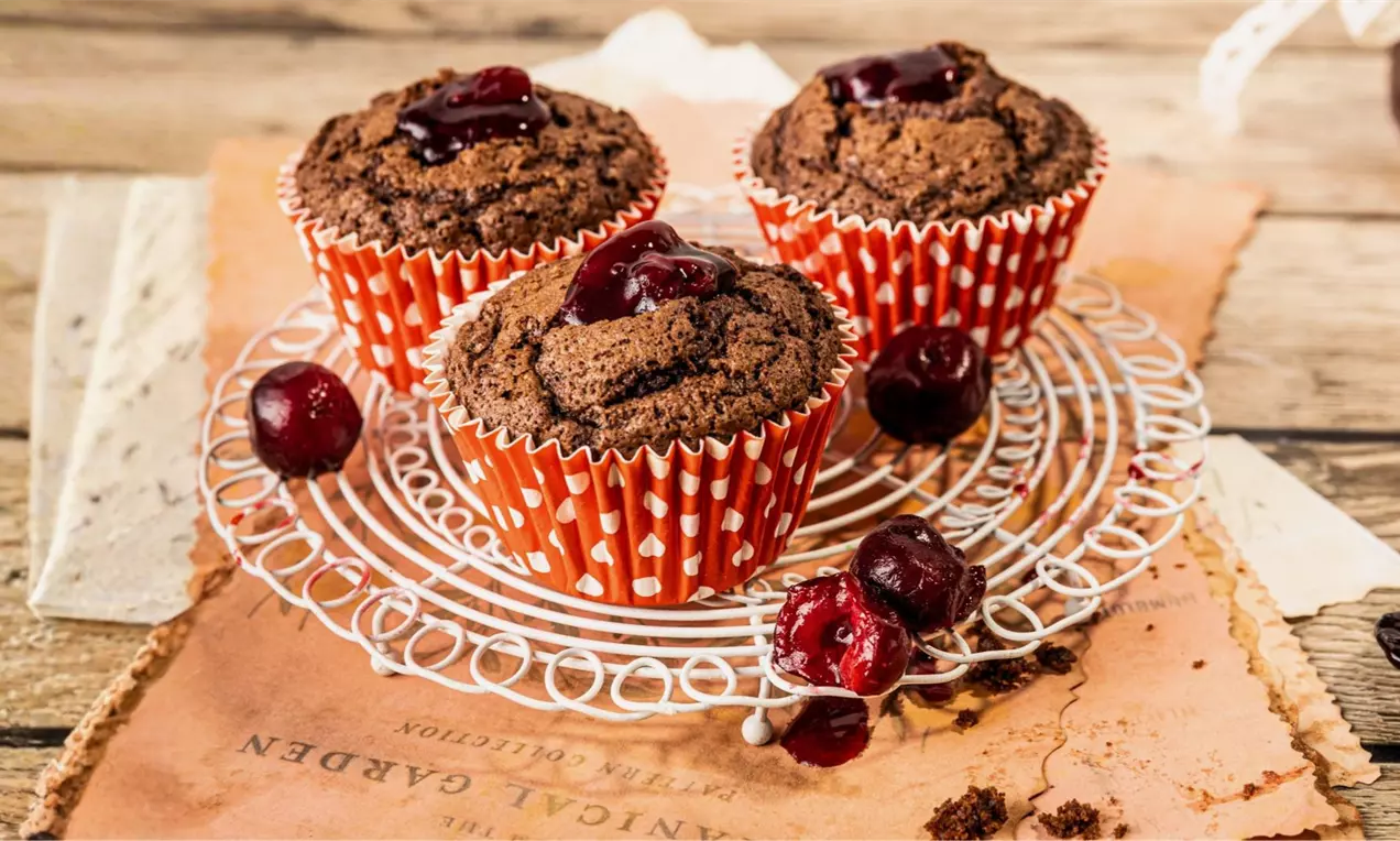 Czekoladowe babeczki podane w papierowych foremkach, udekorowane wiśniami.