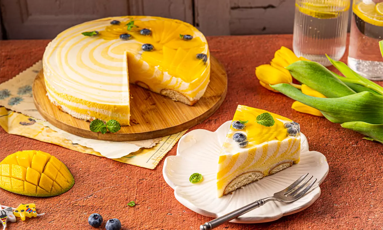 Ciasto piankowe o żółto-białych warstwach, udekorowane soczystymi jagodami, listkami mięty i galaretką, na ceramicznym talerzu