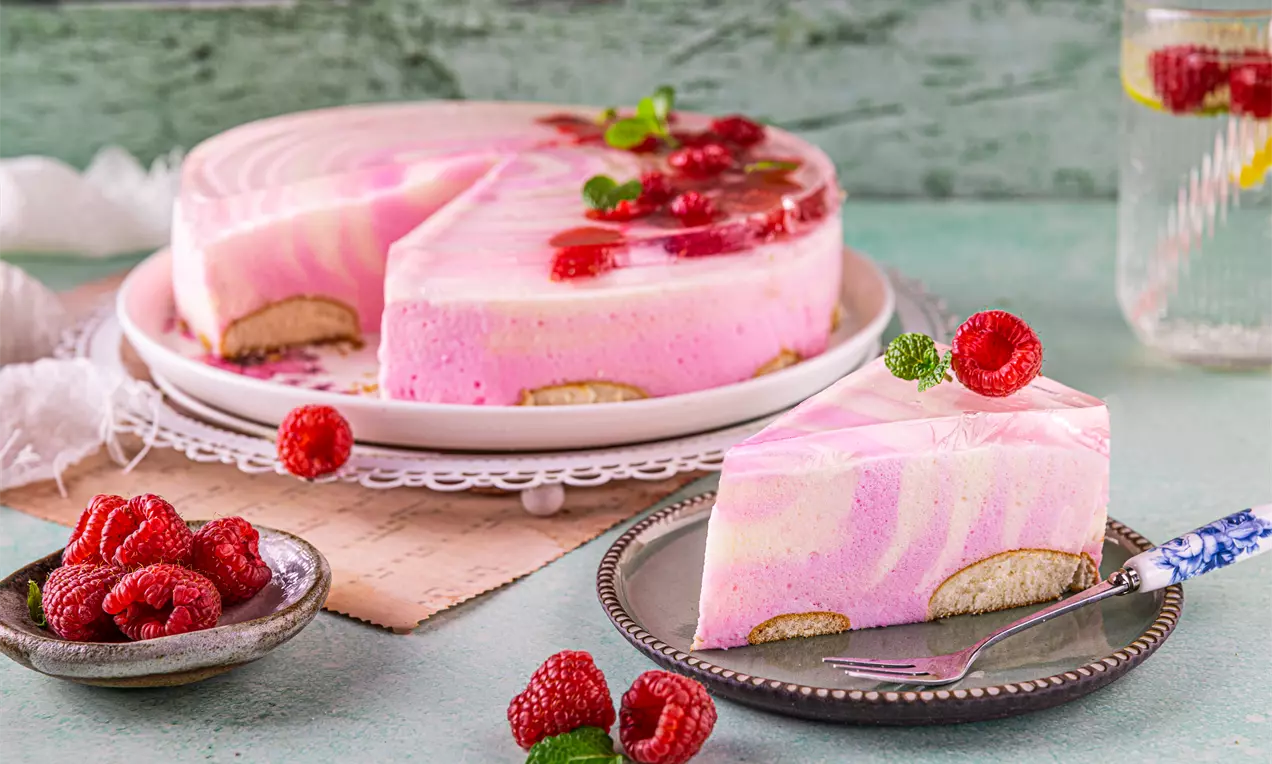 Ciasto piankowe w odcieniach różu z galaretką, malinami i listkami mięty na jasnym talerzu deserowym, podane z malinami na boku