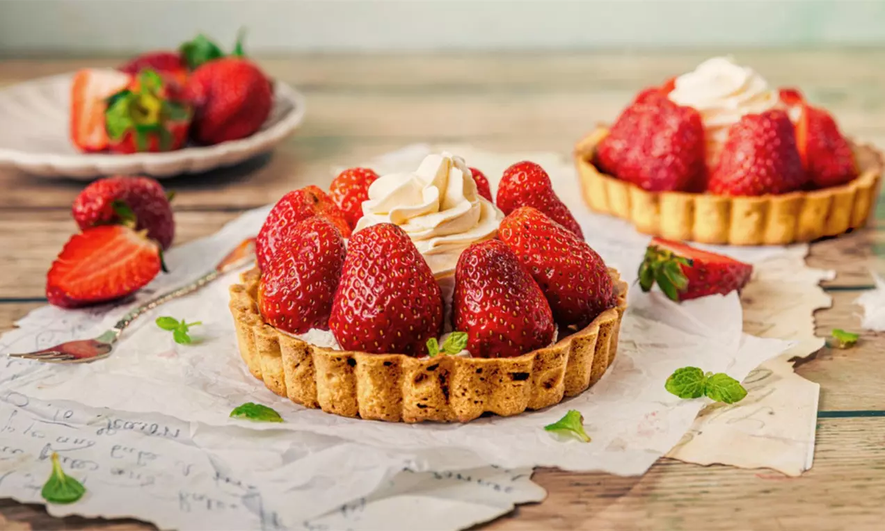 Tartaletki na jasnych talerzach z kremowym nadzieniem, ozdobione całymi soczystymi truskawkami i świeżymi listkami mięty